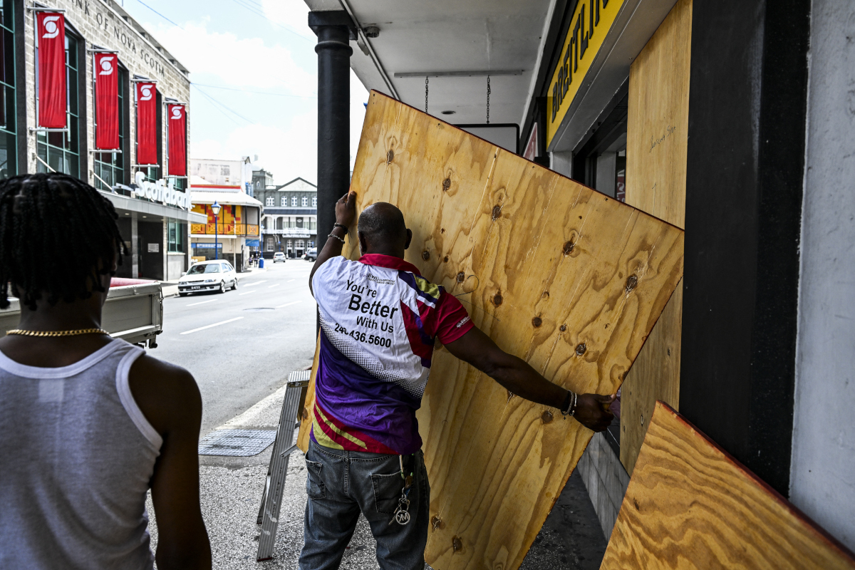 A person nailing a plywood board to a window.