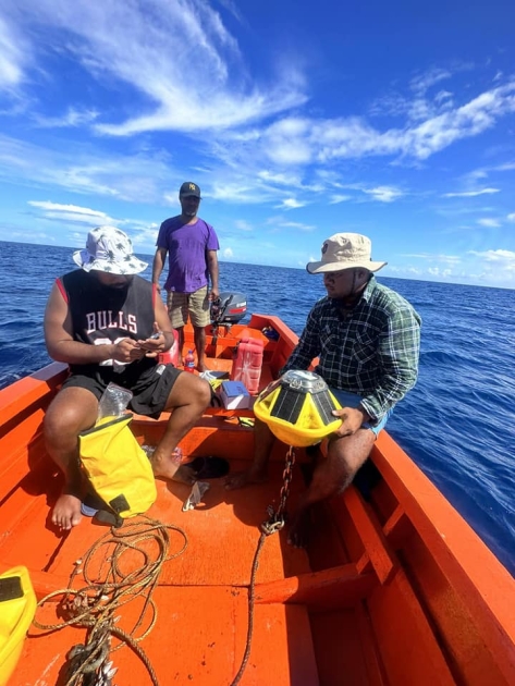 Men in a small boat on the open ocean holding a bright yellow buoy